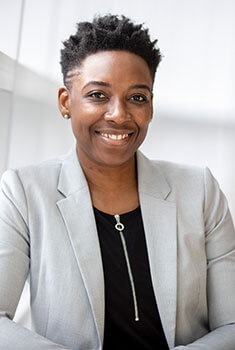 A woman in a suit and black shirt sitting on a chair.