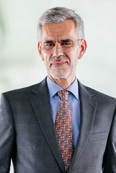 An elderly gentleman in formal attire, standing in front of a wall.