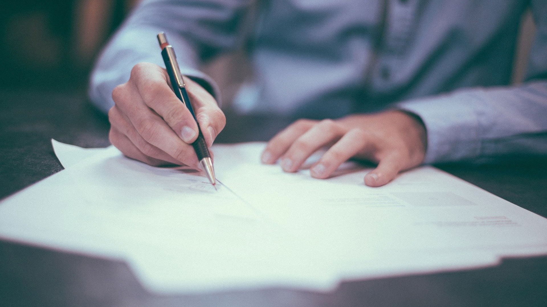 A person writing on a piece of paper with a pen.