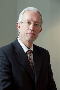A professional man in formal attire posing in front of a wall.