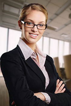 A professional woman in glasses and a business suit standing in an office.