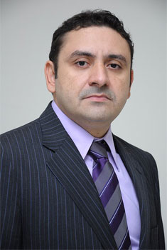 A man in a suit and tie standing in front of a gray background.
